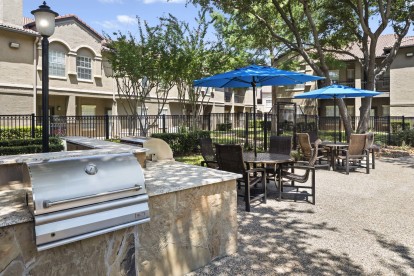 Poolside grills and umbrella-covered seating at Camden Cimarron apartments in Irving, TX