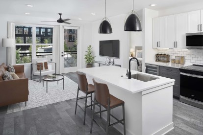 Open kitchen and living space with island, private balcony, and wood-style flooring at Camden Durham apartments in Durham, NC.