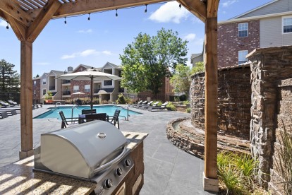 Covered grilling area near pool with water feature and dining table 