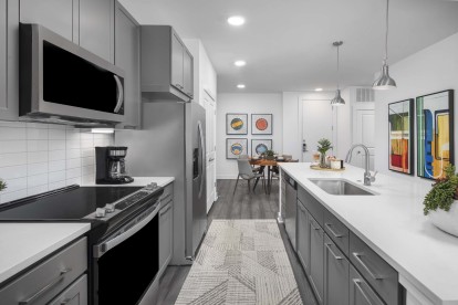 Camden Tempe West Apartments in Tempe Arizona luxury kitchen with stainless steel appliances white quartz countertop gray cabinetry and wood-like flooring, white subway tile backsplash and under cabinet lighting near dining area