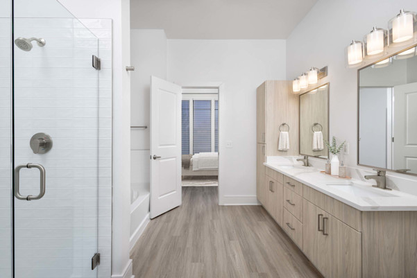 Townhome primary bathroom with double vanity, white quartz countertops, soaking bathtub, and glass-door shower at Camden Belmont apartments in Dallas, TX