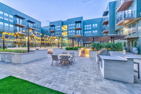 Courtyard at twilight with lit patio string lights and grill area at Camden Greenville apartments in Dallas, TX