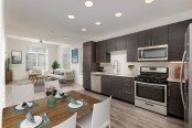 Modern kitchen with white quartz countertops, stainless steel appliances, wood-style flooring, and warm brown cabinetry 