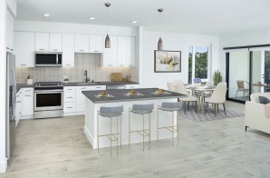 Open concept kitchen with stainless steel appliances, space for bar stool seating, dining area, and patio