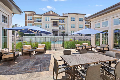 Patio deck lounge with large umbrella-covered seating by the pool at Camden La Frontera apartments in Round Rock, TX