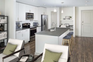 Kitchen with large island, gray countertops, light wood cabinetry, single-basin sink, stainless steel appliances and built-in desk.