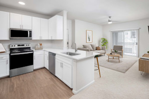 Modern kitchen with stainless steel appliances, white cabinetry, white quartz countertops and open-concept floor plan with sliding glass door to the private patio at Camden Spring Creek Apartments in Spring, Tx