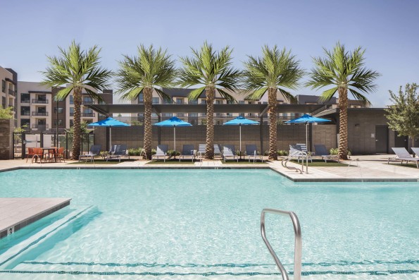 Camden Tempe West Apartments in Tempe Arizona pool close up shot with sun deck and loungers under palm trees and umbrellas