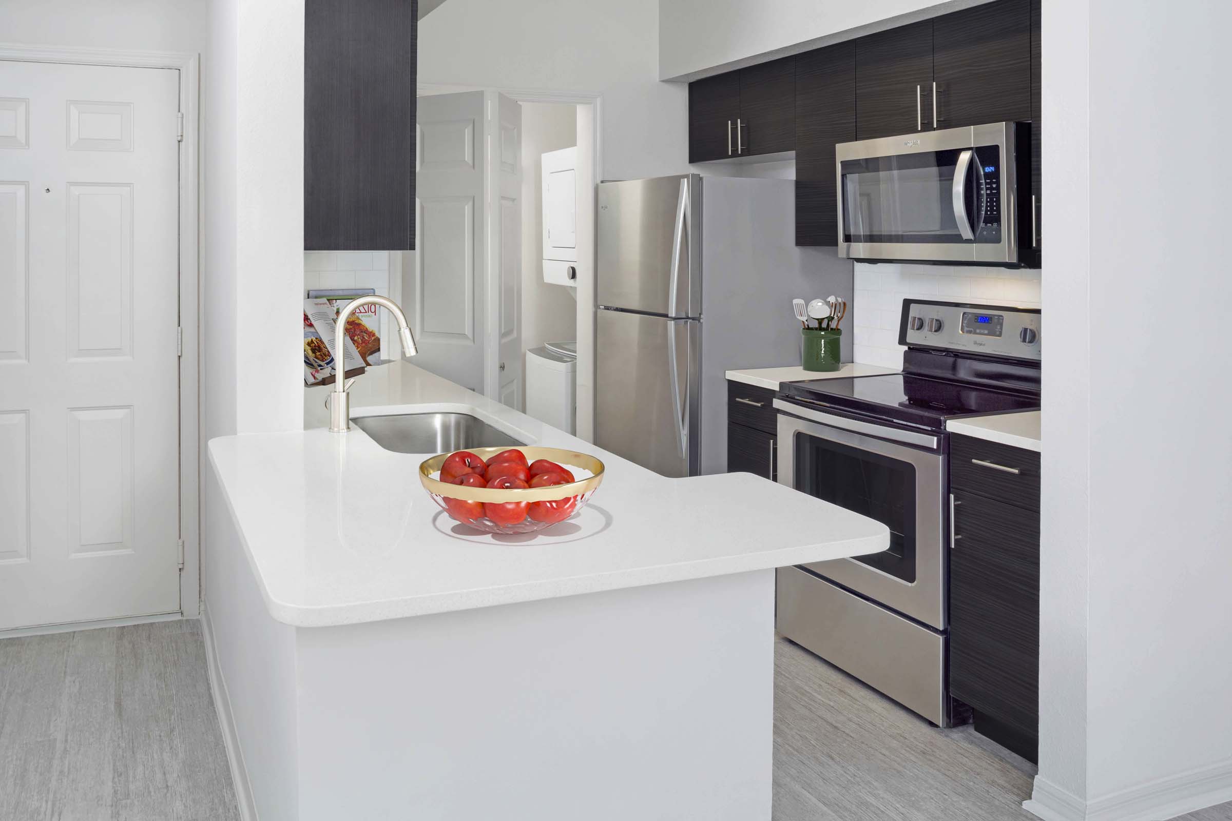 Modern kitchen with white quartz countertops, large breakfast bar, soft close cabinets, and stainless steel appliances at Camden Lee Vista apartments in Orlando, FL