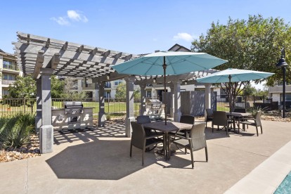 Poolside grilling cabana and seating with light blue umbrellas at Camden Cedar Hills apartments in Austin, TX