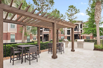 Outdoor grilling area with seating by the pool at Camden Grand Harbor Apartments in Katy, Tx