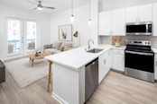 Modern kitchen and living room with white cabinetry, grey subway tile backsplash, white quartz counter tops with grey veining and stainless steel appliances at Camden Travis Street in Midtown Houston, Tx