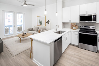 Modern kitchen and living room with white cabinetry, grey subway tile backsplash, white quartz counter tops with grey veining and stainless steel appliances at Camden Travis Street in Midtown Houston, Tx