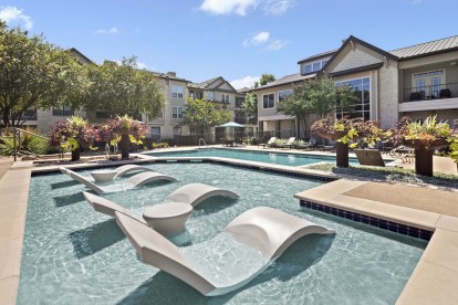 Resort-style pool with in-water loungers and light blue umbrellas at Camden Cedar Hills apartments in Austin, TX