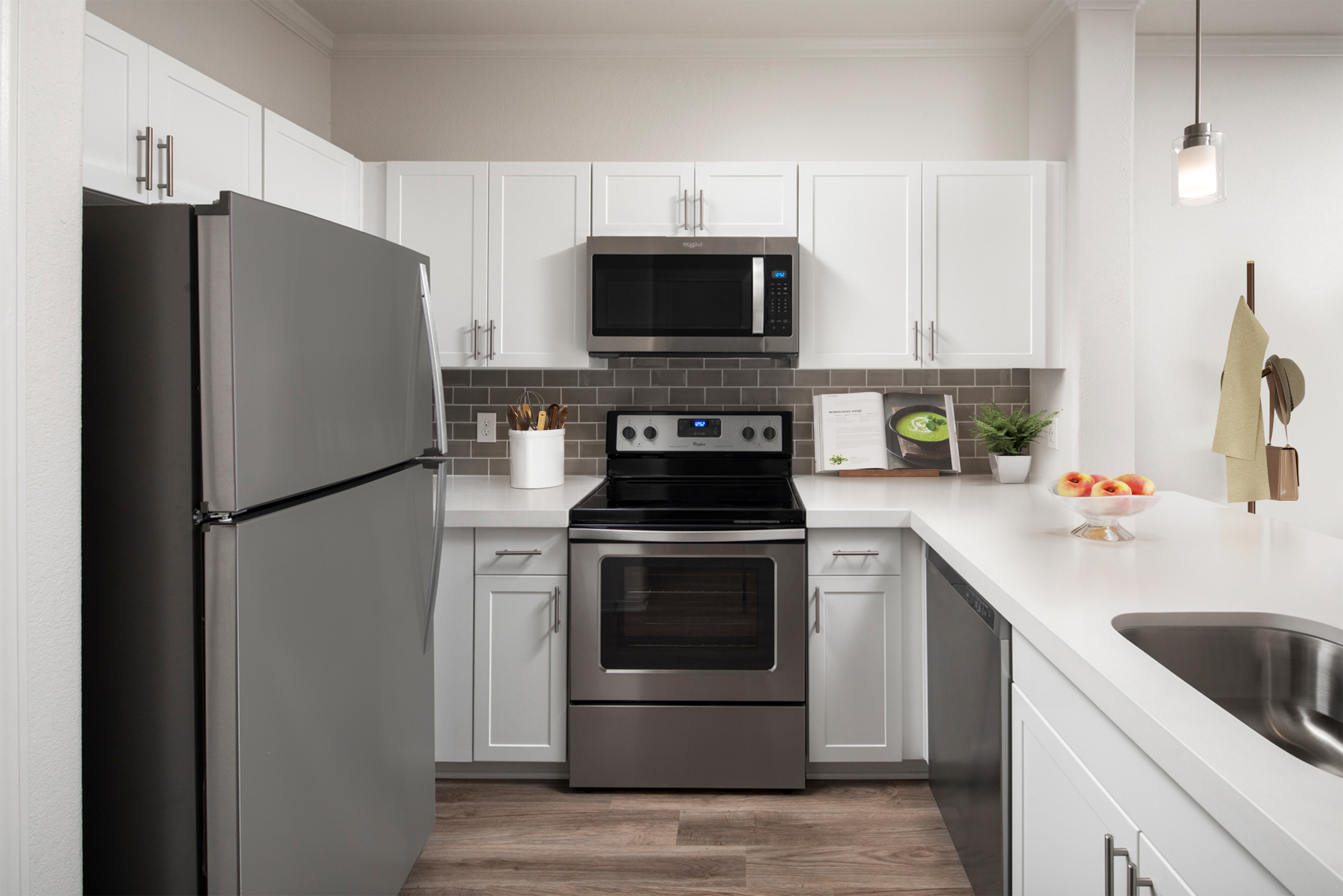 Open-concept kitchen with wood-style flooring, white quartz countertops, white shaker cabinets, gray subway tile backsplash, and stainless steel appliances