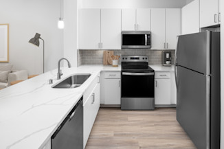 Modern kitchen with white cabinetry, grey subway tile backsplash, white quartz countertops with grey veining and stainless steel appliances at Camden Travis Street in Midtown Houston, Tx