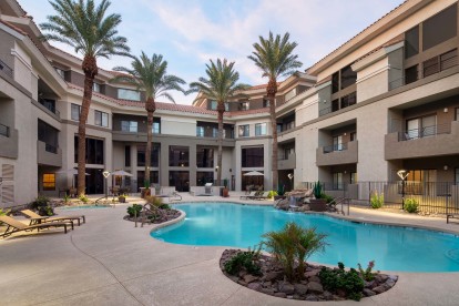 Lighted pool and waterfall with gas grilling stations and dining areas at dusk