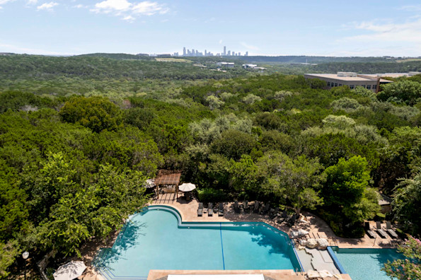 Resort-style pool surrounded by trees with downtown Austin on the horizon at Camden Gaines Ranch apartments in Austin, TX