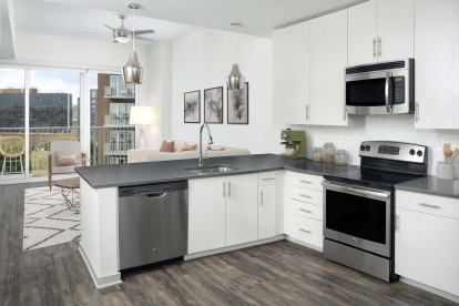 Kitchen with light cabinets, gray countertops, white backsplash, stainless steel appliances, wood-style flooring throughout and private balcony