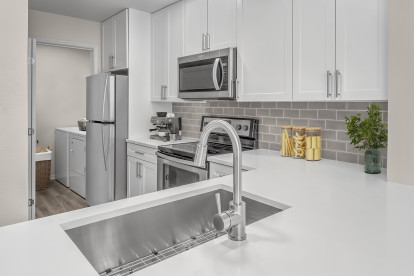 Kitchen with white quartz countertops and white cabinetry with adjacent laundry room