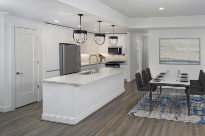 White contemporary kitchen and dining room with hardwood-style flooring, pendant lighting, and white quartz countertops and whit