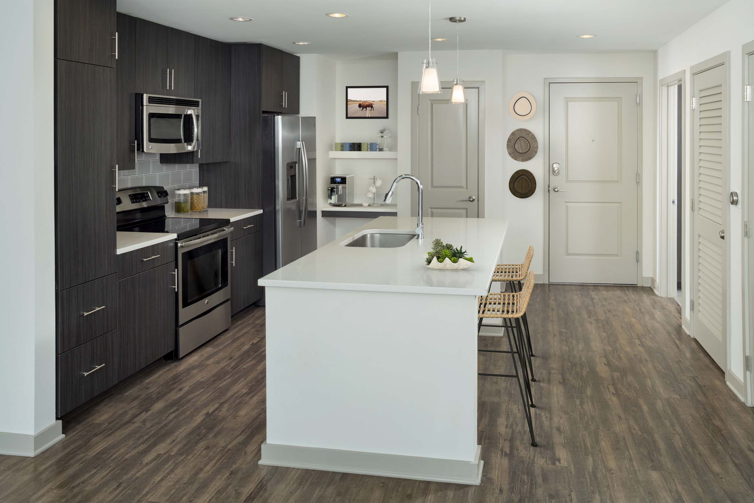 Kitchen with large island, light quartz countertops, brown cabinetry, stainless steel appliances, single-basin sink and built-in bar.