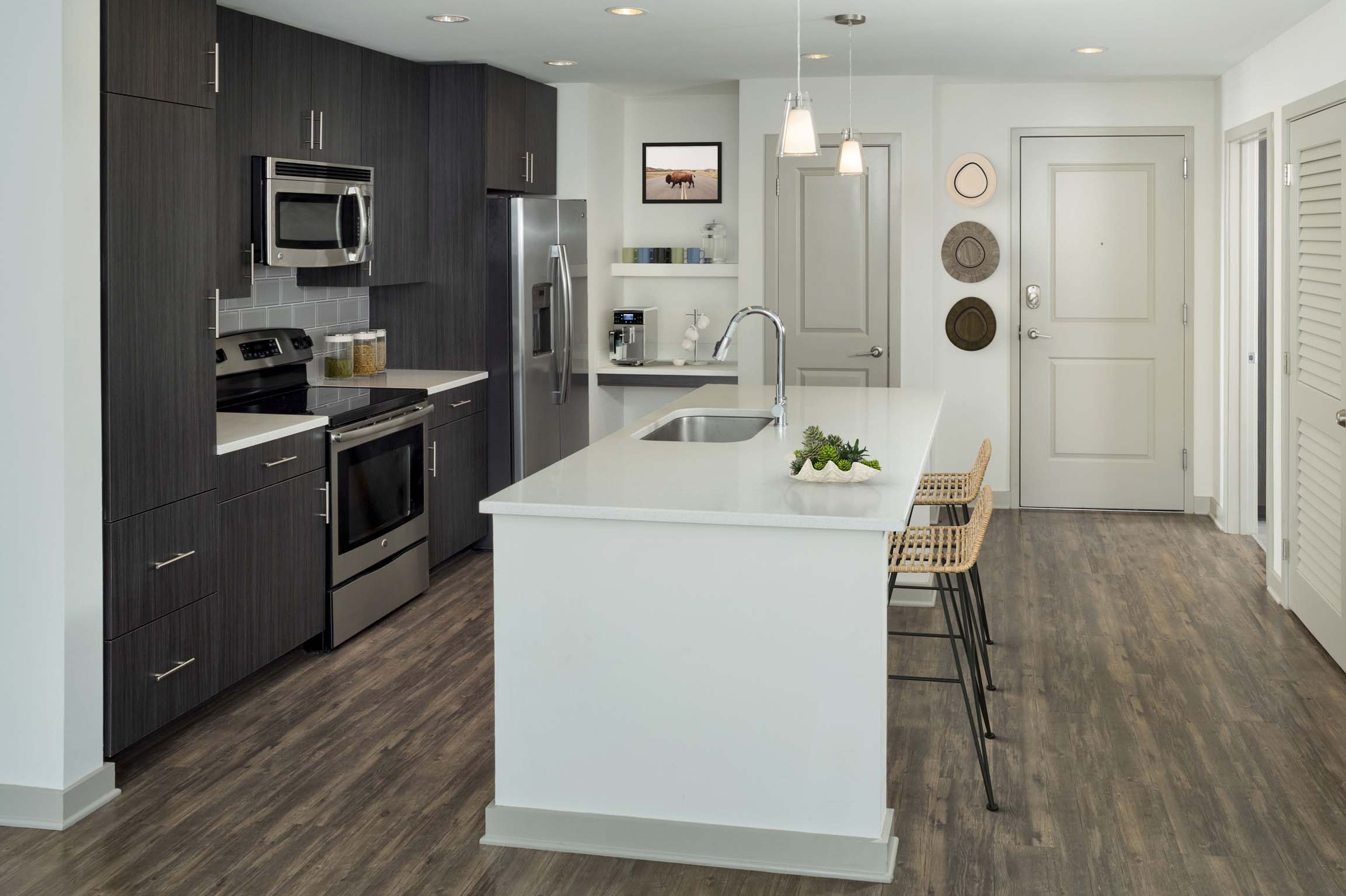 Kitchen with large island, light quartz countertops, brown cabinetry, stainless steel appliances, single-basin sink and built-in bar.
