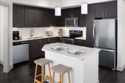 Beautiful open kitchen with stainless steel appliances, quartz countertops, tile backsplash, pull down spray faucet, espresso color cabinetry with brushed nickel hardware, and LED pendant lighting at Camden Boca Raton apartments in Boca Raton, Florida.