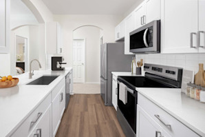 A contemporary style kitchen with stainless steel appliances, white quartz countertops, and a glass cooktop at Camden Overlook apartments in Raleigh, NC. 