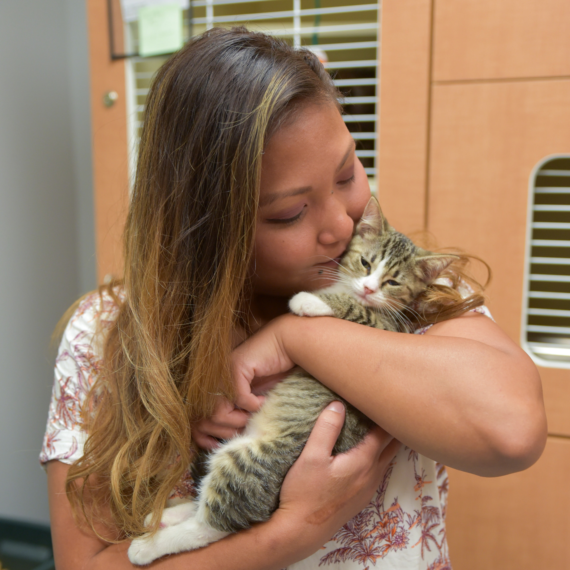 A woman hugs and kisses a kitten in her arms.