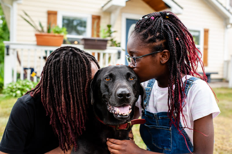 Two people kissing their dog outside.