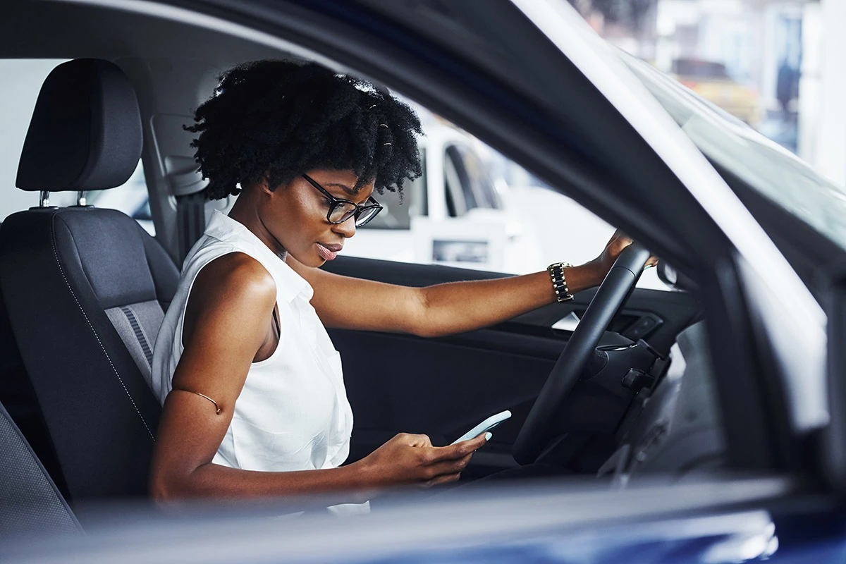 Woman sits in her car and checks her phone