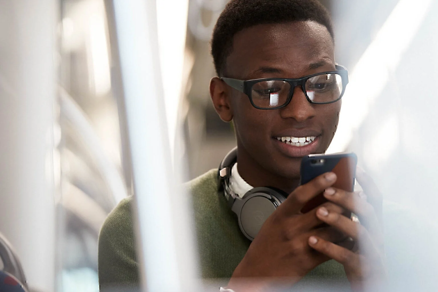 Man grinning while looking at his smartphone on the subway