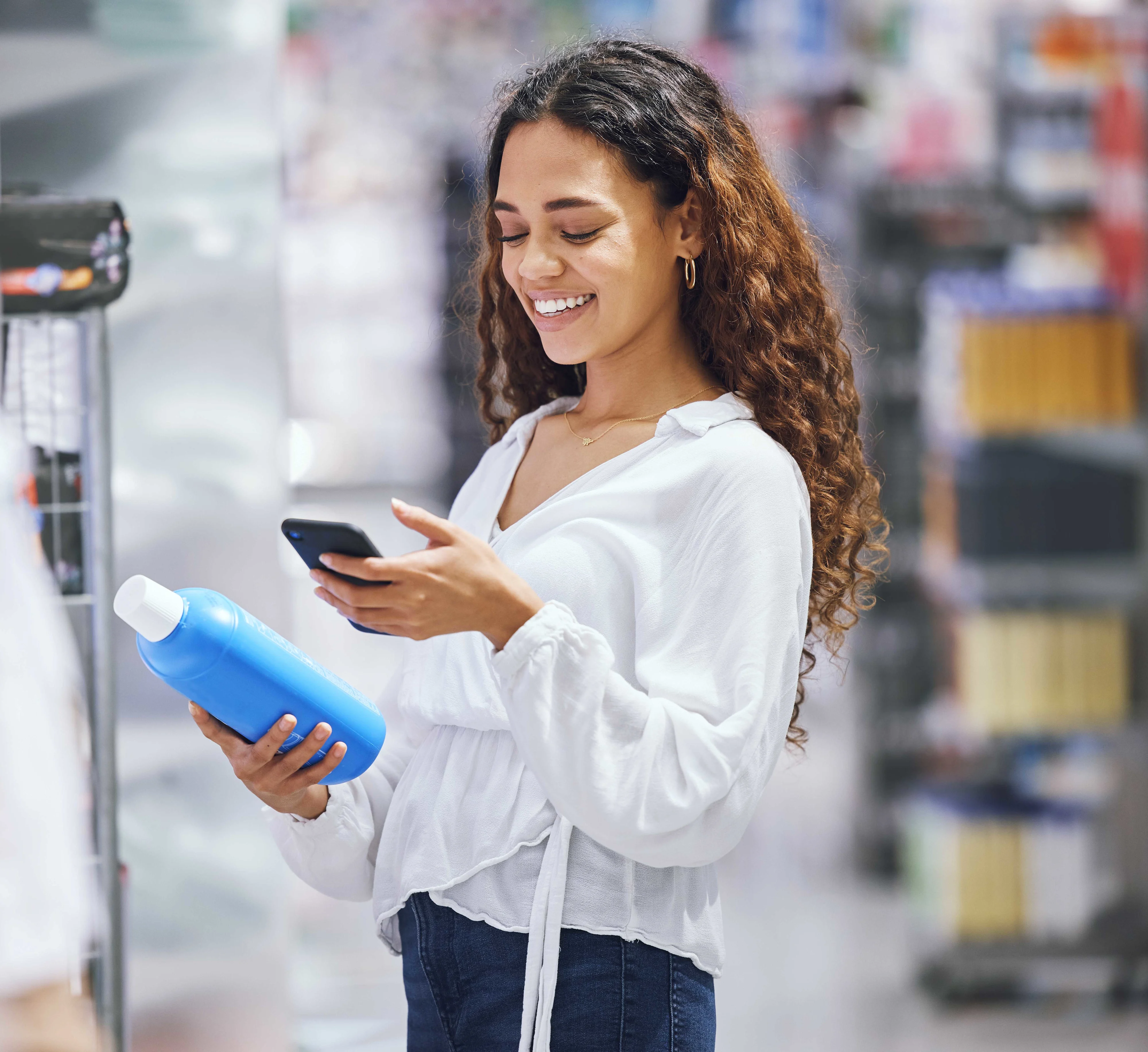 A woman in a retail store holding a water bottle while checking her phone.
