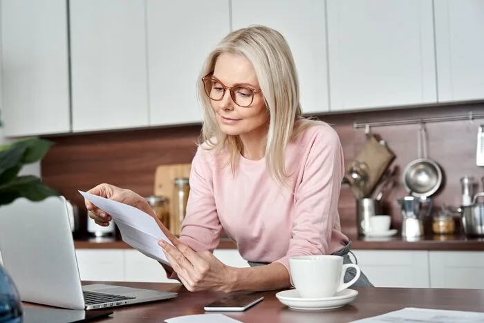 Woman reading paper letter bill sitting at home kitchen