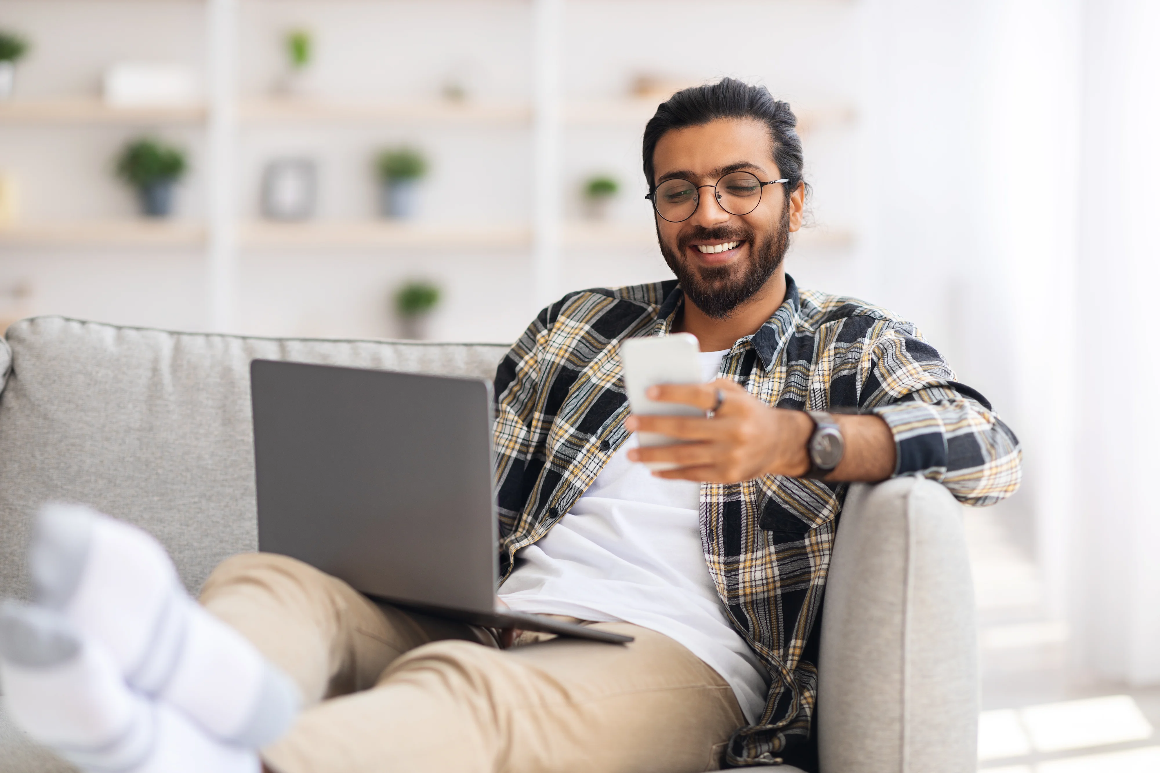 Indian man sitting on sofa with laptop and phone