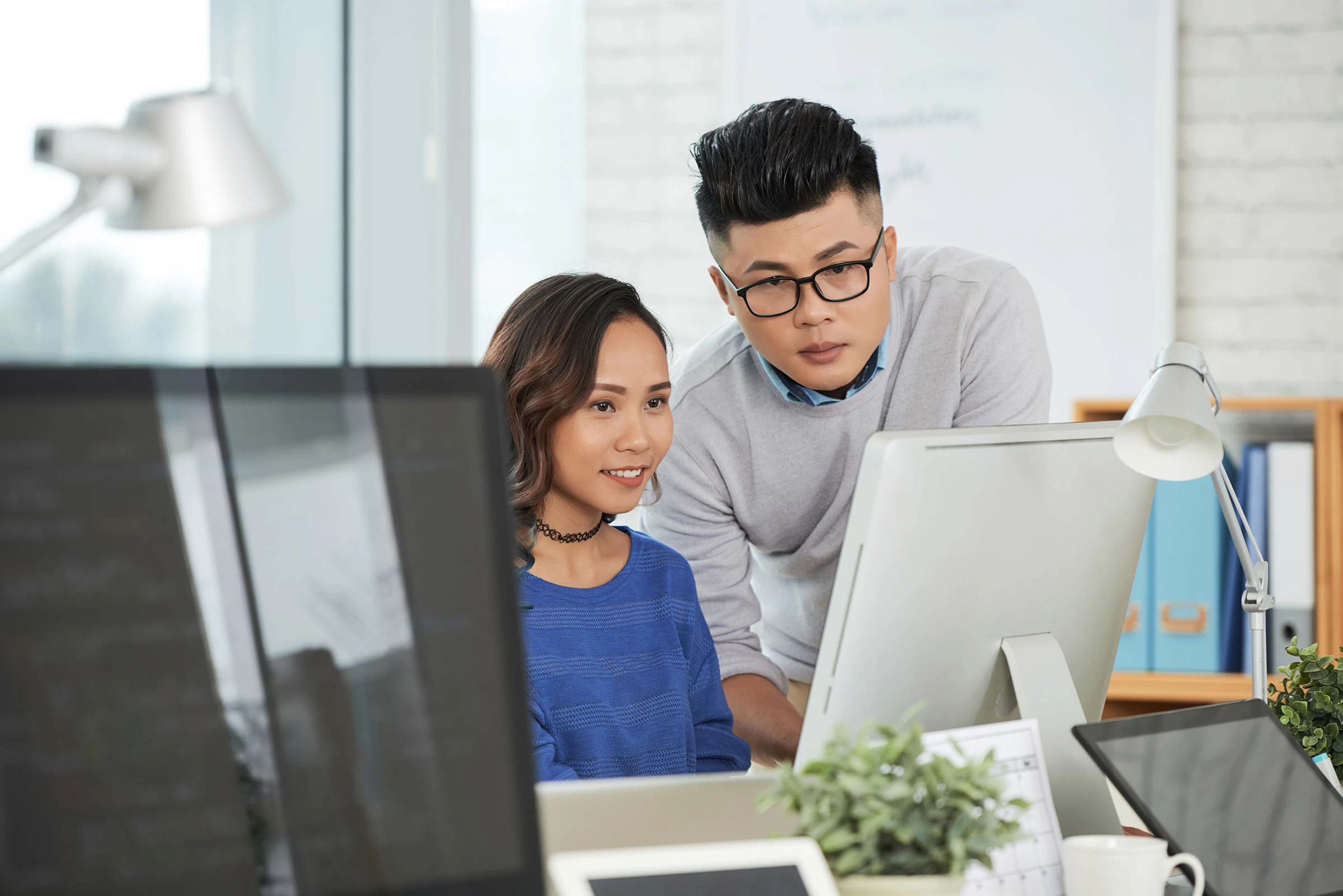 Two colleagues collaborate at a computer in the office.