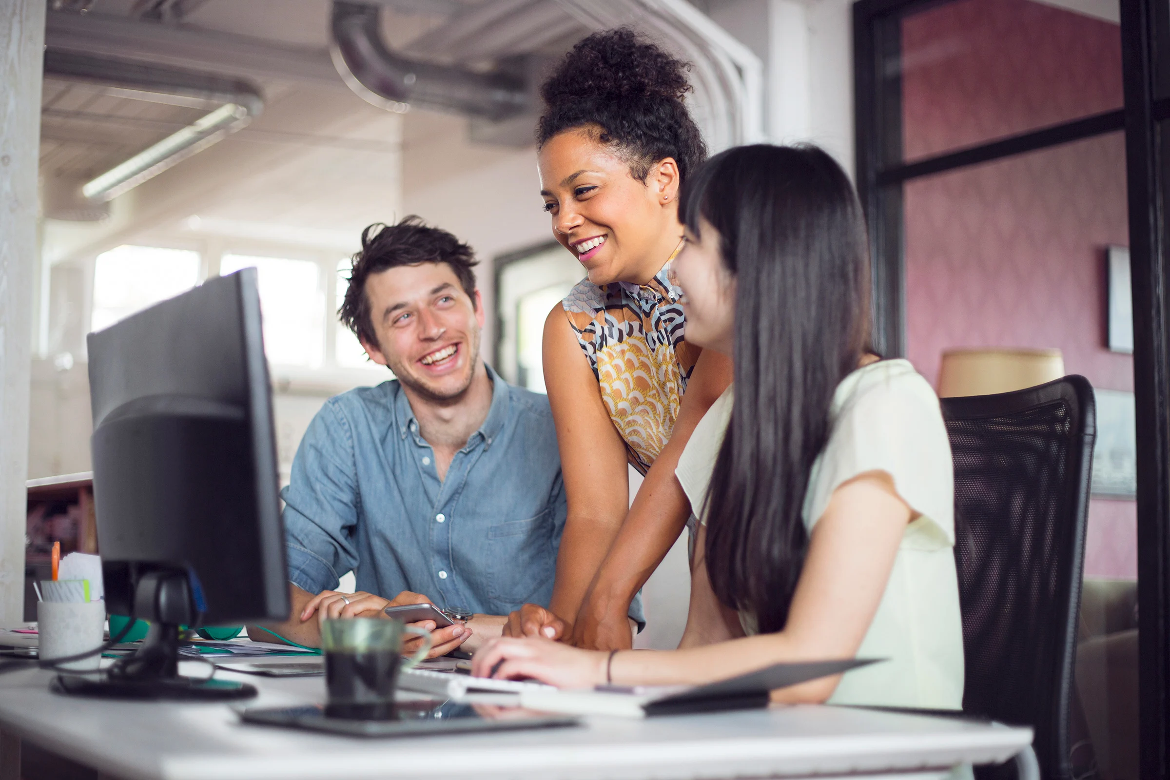coworkers smiling in front of computer monitor