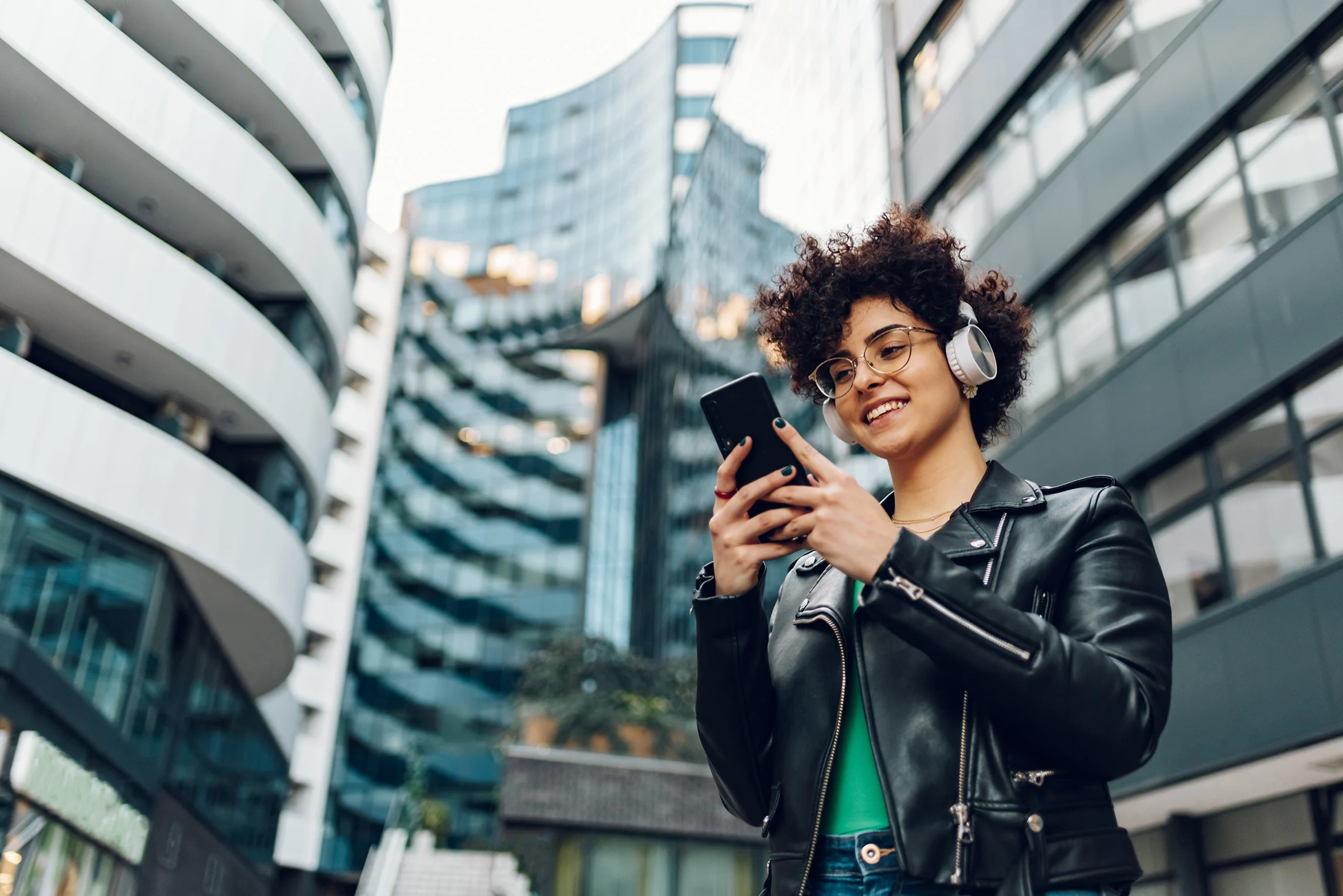 Woman walking in the city streets and using smartphone and headphones