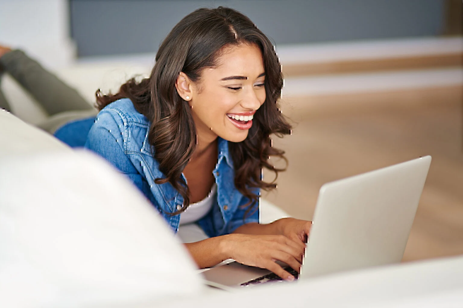 woman laying on couch smiling at laptop