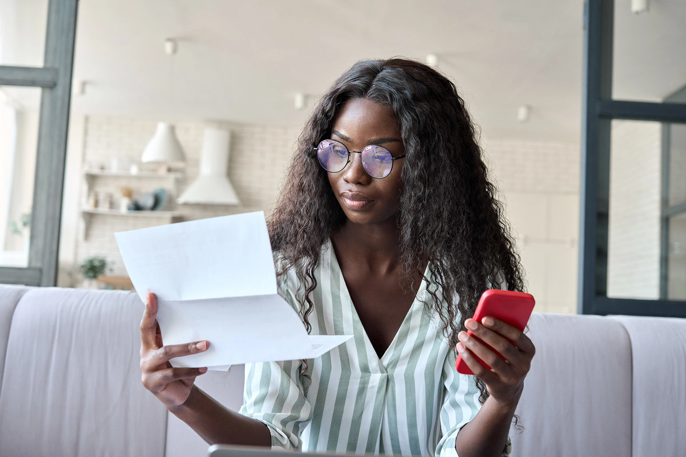 Young serious African American businesswoman reading letter using cellphone.