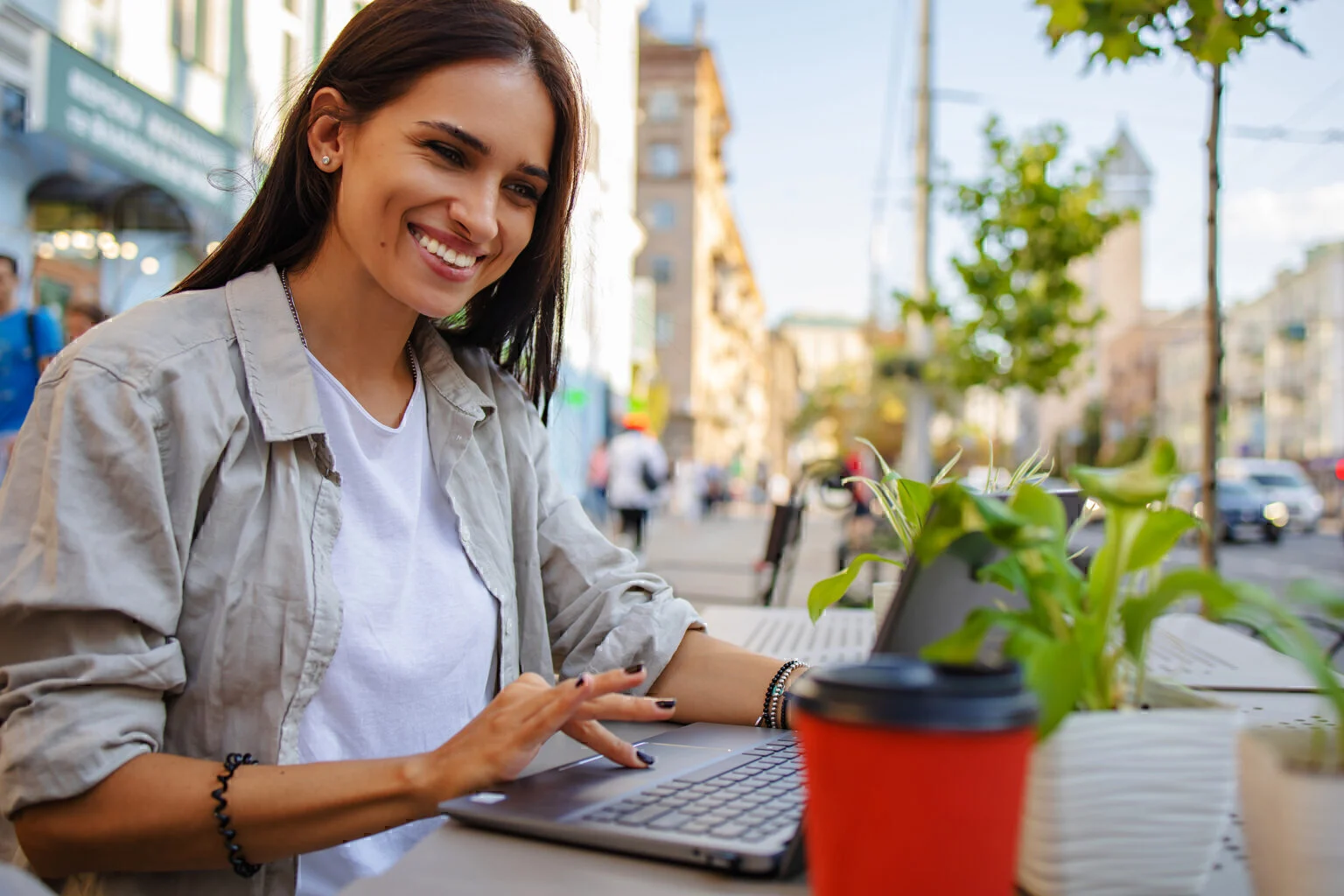Happy beautiful woman with laptop near hi-tech business building. She drinks coffee in to go cup