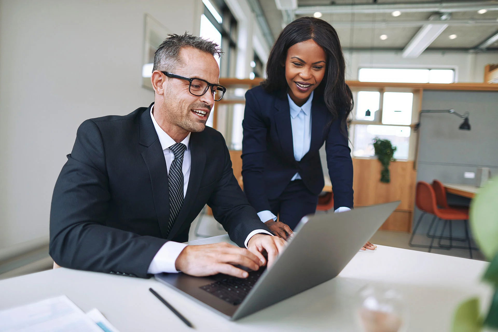 Two Diverse Businesspeople Smiling And Talking Together While Working On A Laptop At A Table