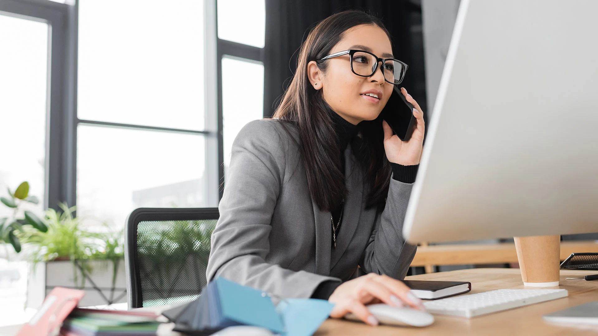 Young asian business woman talking on mobile phone and using computer in office