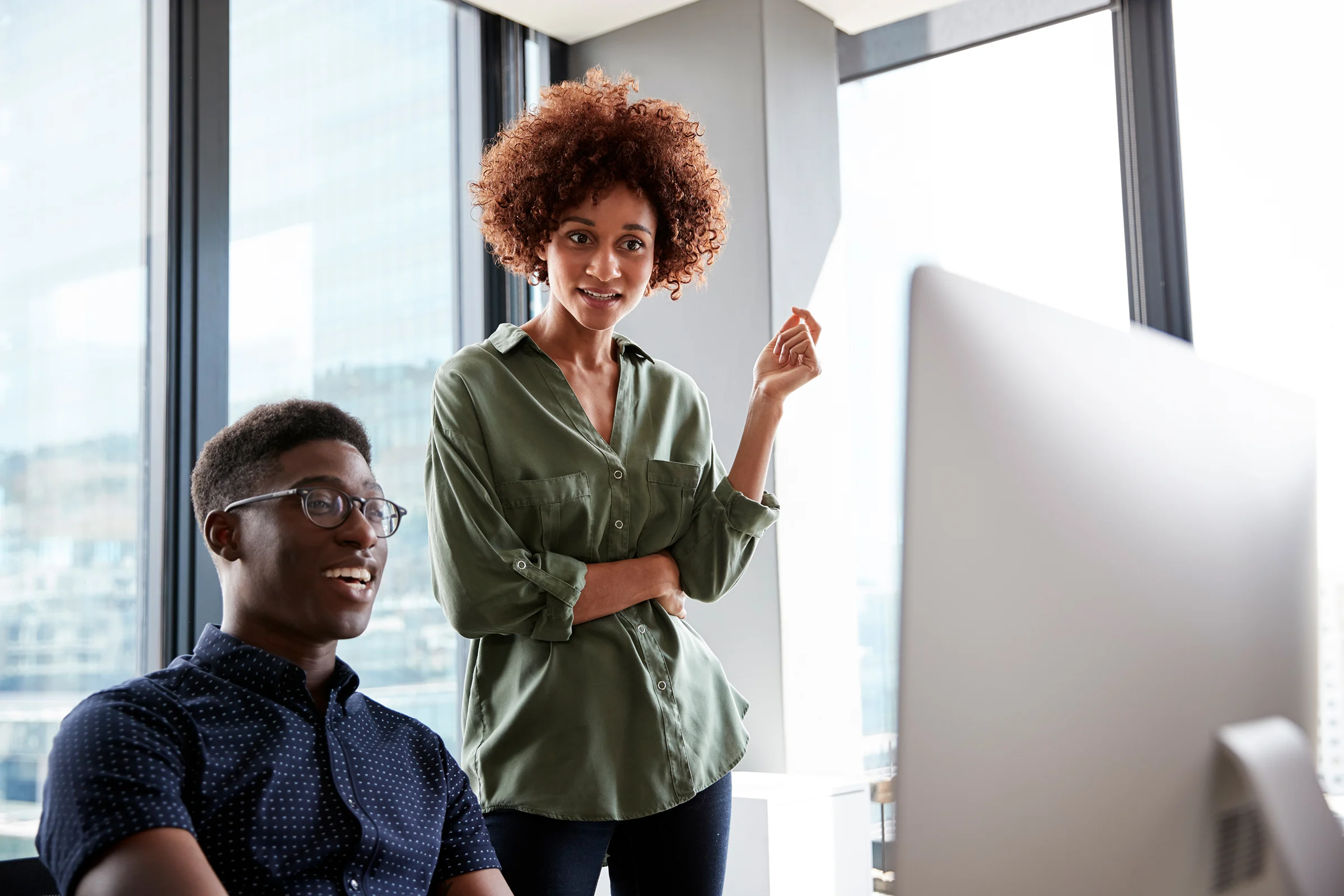 A male and female creative working together at a desk looking at a computer monitor, close up