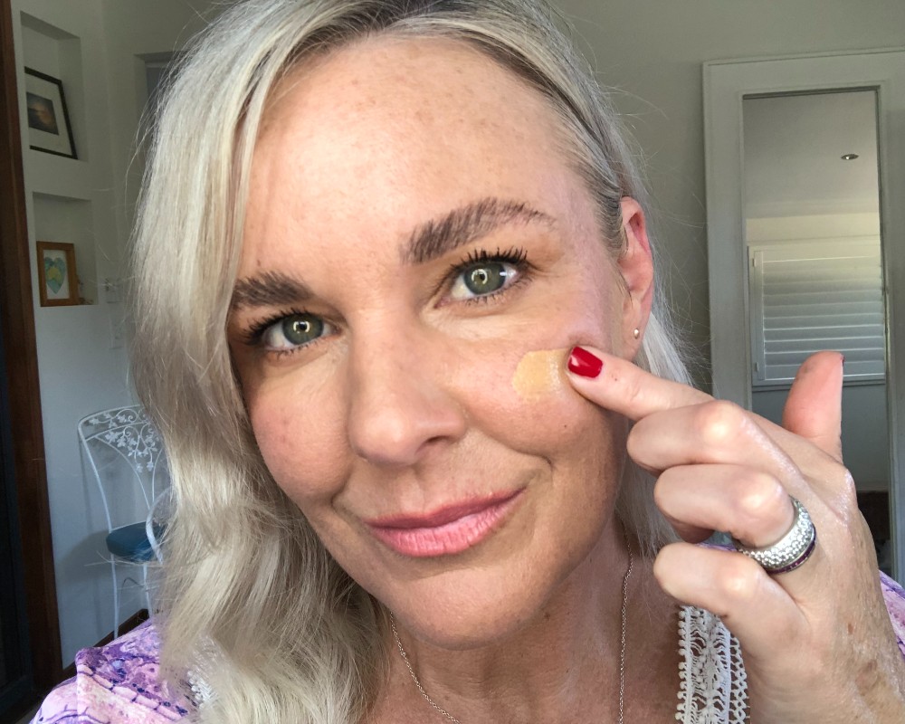 best primer for mature skin australia_woman in her 50s using finger to apply tinted primer to her cheek