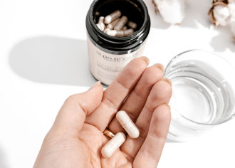 Apotecari Mane Event - two supplement tablets sit in the palm of a hand. In the background is a glass of water and jar of Apotecari Mane Event - 1080 x 771