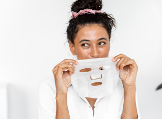 best-face-masks-for-acne-scars_a woman is holding a sheek mask up above her mouth as she playfully looks to the side - 1080 x 800 