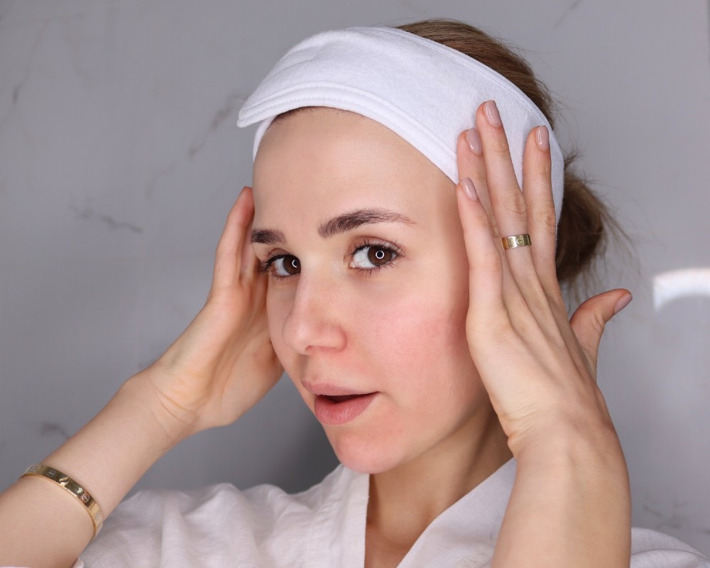 How To Hydrate Your Skin With Weleda Skin Food_woman in bathroom with headband on to tie her hair back before applying skin care rotuine