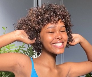 What Products Can Make My Frizzy Hair Look Smoother?_a woman is grinning as she holds up her curly hair_1080x900